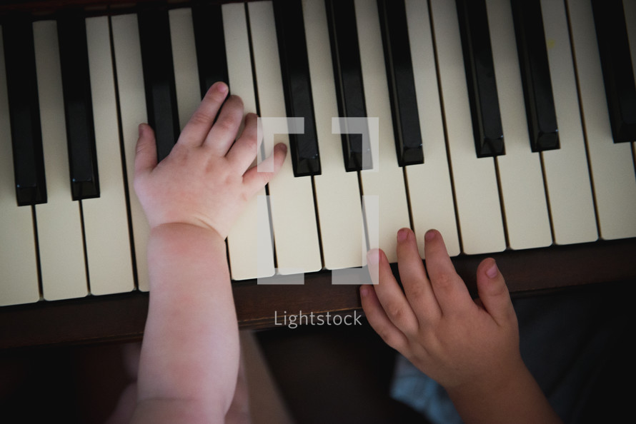 infant and toddler hands on a piano 