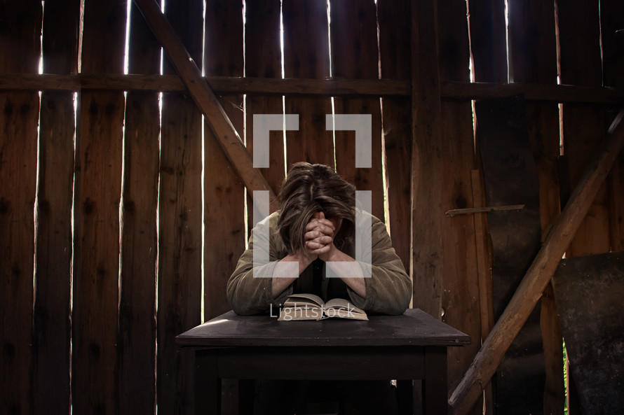 a man kneeling and praying over a Bible in a barn 