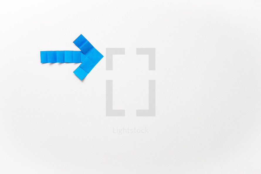 A blue arrow made of squares of paper on a white background.