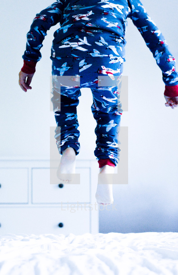 a boy in pajamas jumping on a bed 