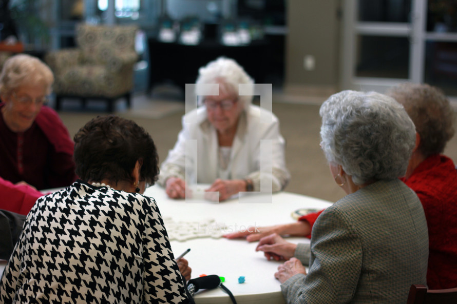 Seniors playing dominoes at a round table.