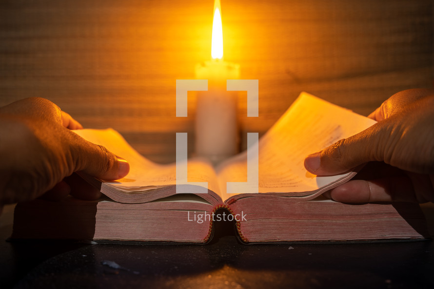 candle light with hands reading bible on wooden table in the night time.