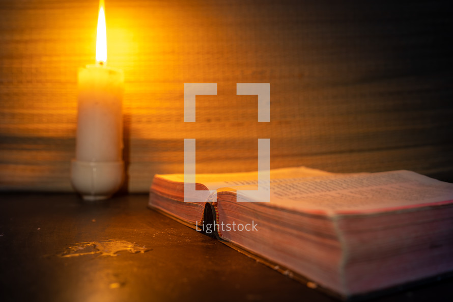 candle light and holy bible on wooden table in the night time.