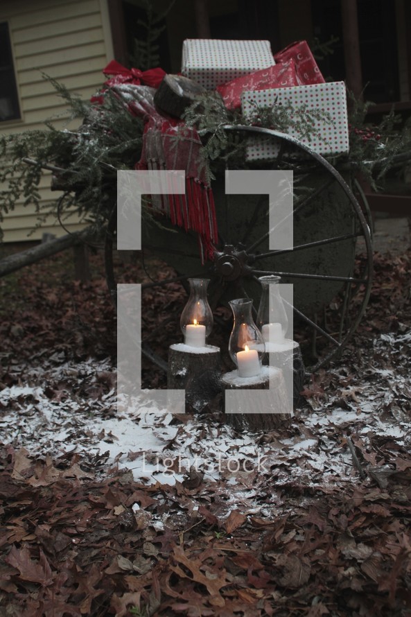 candles burning in glass lanterns in front of a carriage wagon full of presents dusted with snow