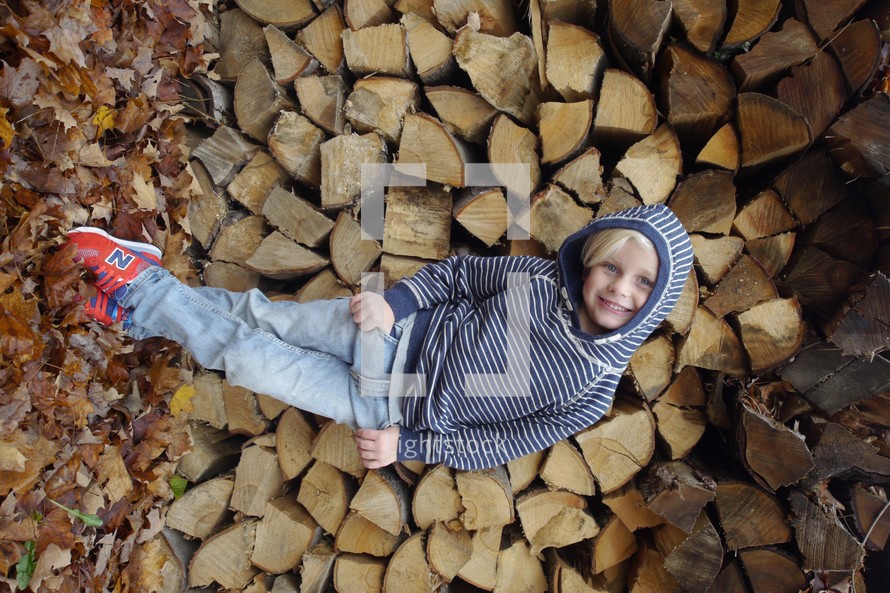 child in front of a stack of fire wood 