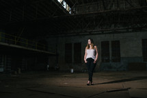 a young woman standing in an abandoned warehouse 