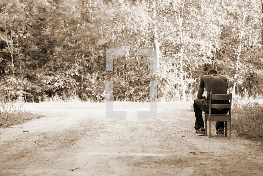 man sitting on a chair on a dirt road 