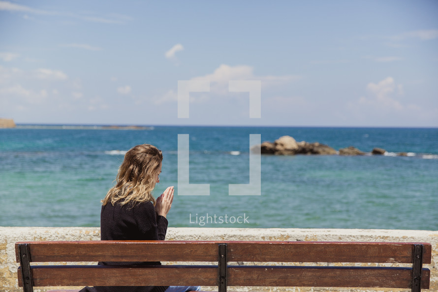 woman saying a prayer sitting on a bench on a beach in Greece 