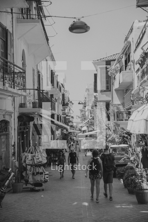 pedestrians walking on a narrow street lined with shops in Greece 