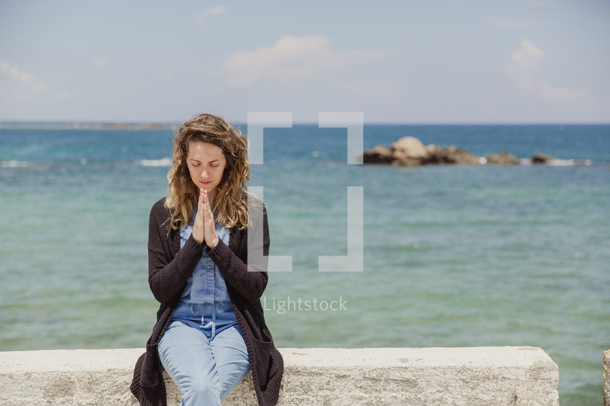 man in prayer sitting on a wall at the coast in Greece