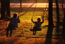 kids on a swing set at sunset 