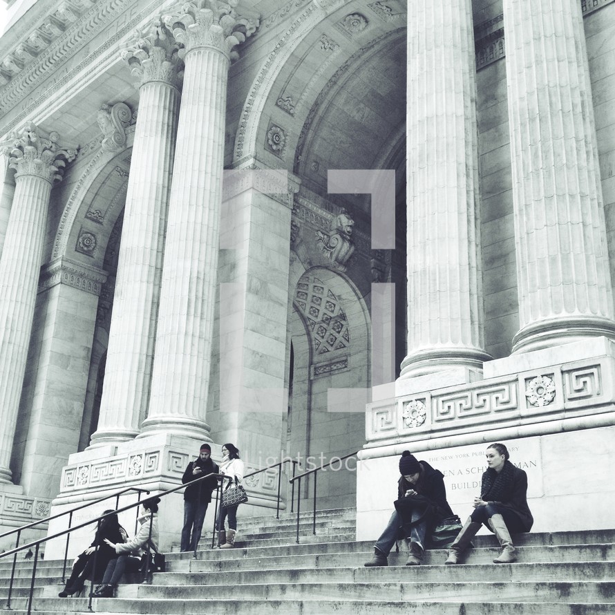 people sitting on the stairs in front of a building with large columns and arches 