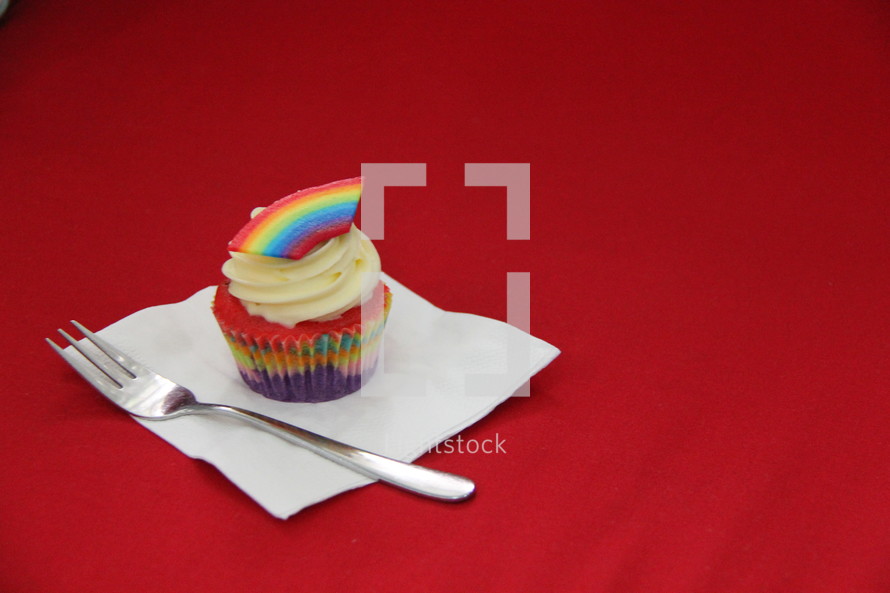 Cupcake decorated with cream cheese, sprinkles and a fondant rainbow 