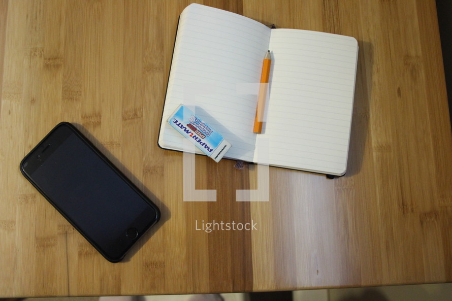 open journal, cellphone, pencil, and eraser on a desk 