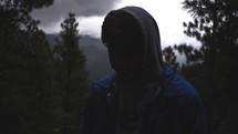 man in a hoodie looking down in a forest 