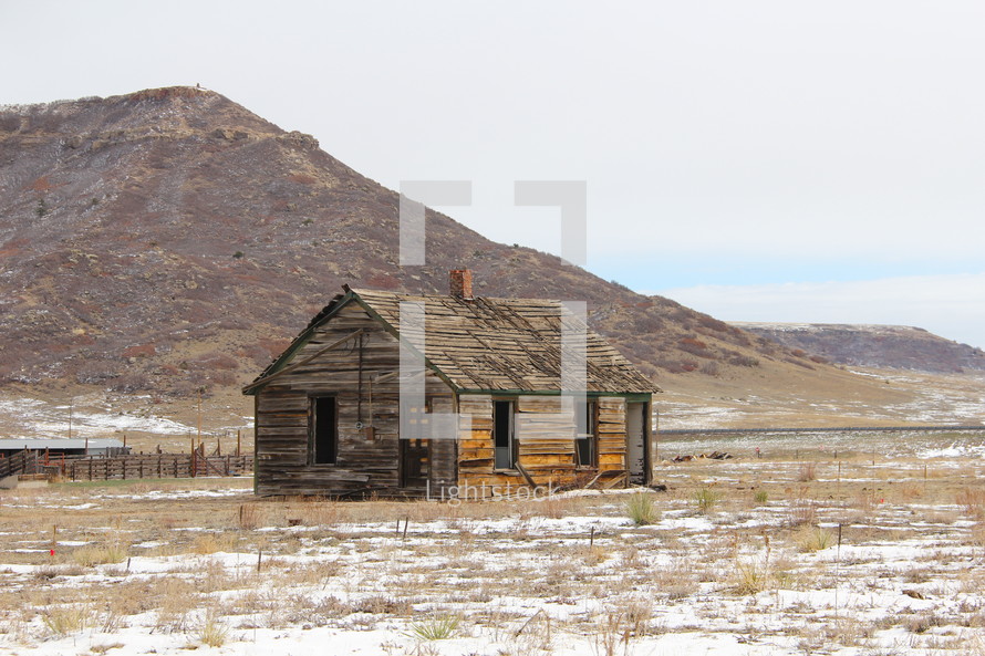 Derelict log cabin on snow covered plain at the foot of the rocky mountains