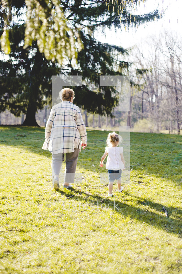 a grandmother and granddaughter walking up a grassy hill 