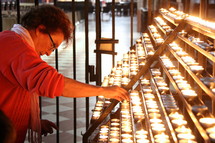 Lady saying a prayer and lighting a votive or prayer candle in a Catholic Cathedral.