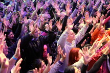 Worshippers with arms raised at a church service. People making a decision for Christ at an evangelistic outreach.