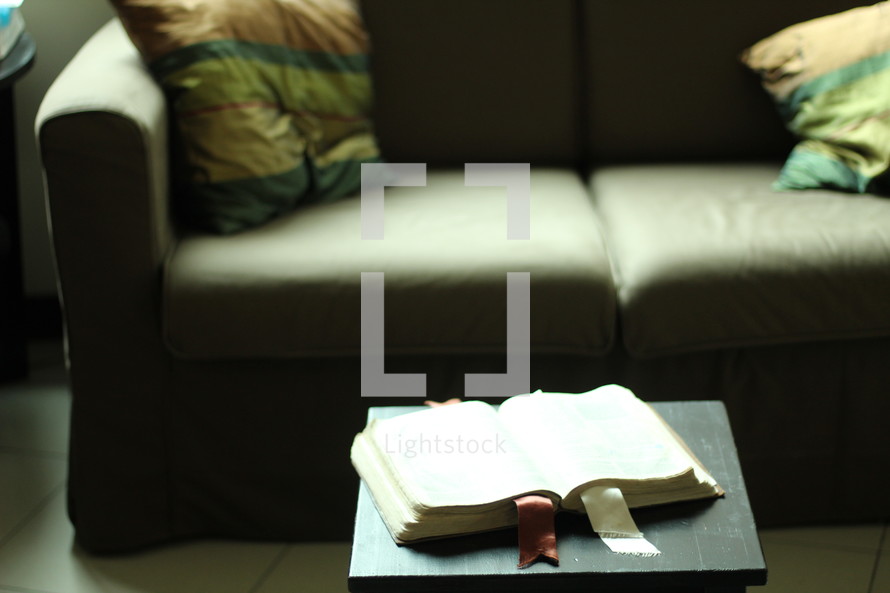 an open Bible on a coffee table in front of a couch 
