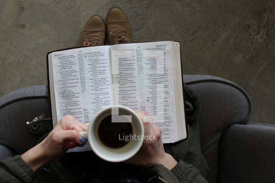 a woman reading a Bible in her lap and holding a coffee mug 