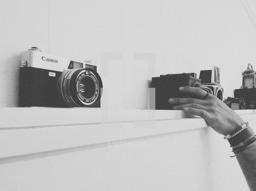 Hand placing vintage cameras on a shelf.