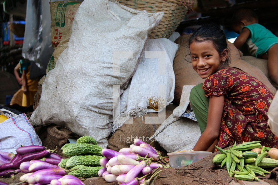 Lower caste Hindu girl sorts vegetables in a city market [For similar search Ethnic Smile Face]