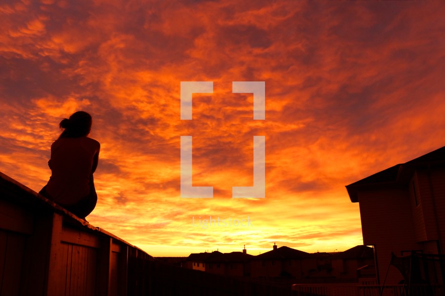 woman sitting outdoors under an orange sky at sunset 