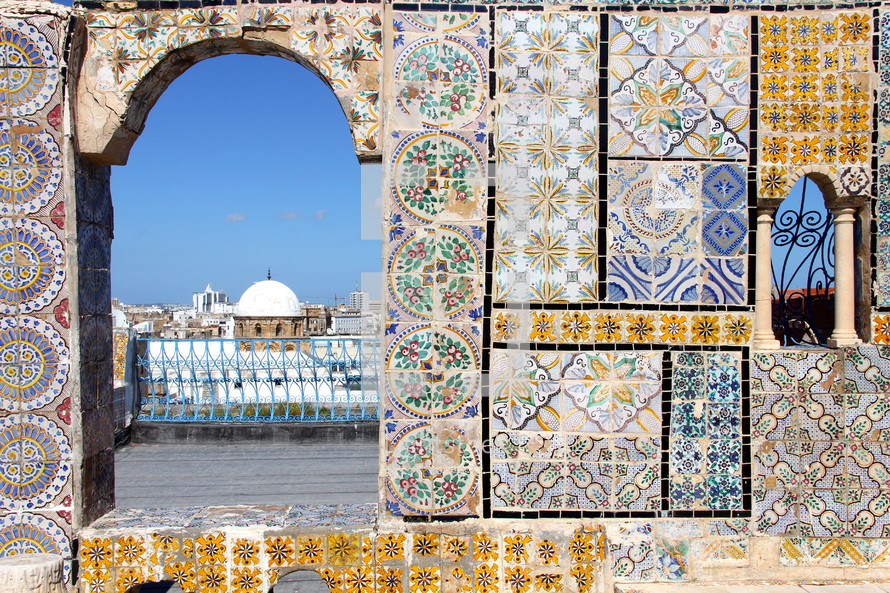 View of a domed mosque in an Arab city in North Africa through a decorative tiled archway.