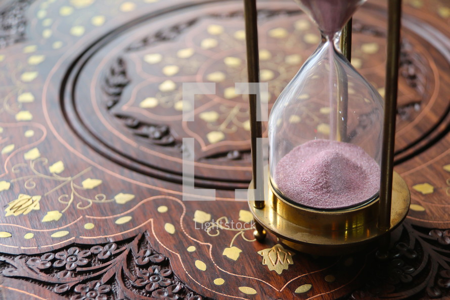 Sand measuring time running through an antique hour glass on oriental desk