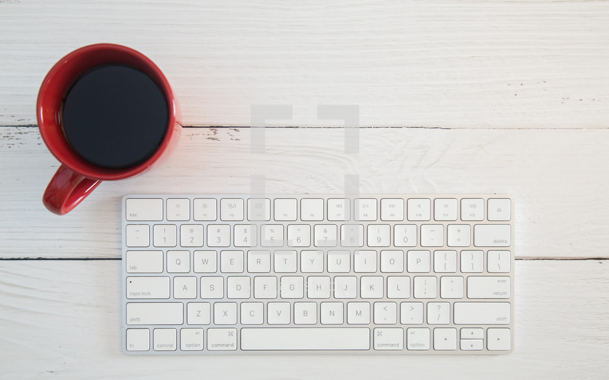 wireless computer keyboard and coffee mug on a white wood table 