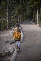 a girl walking on a dirt path through a forest 