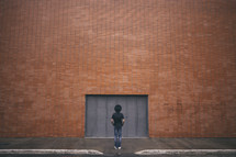 man standing with his back to the camera and a brick warehouse building 