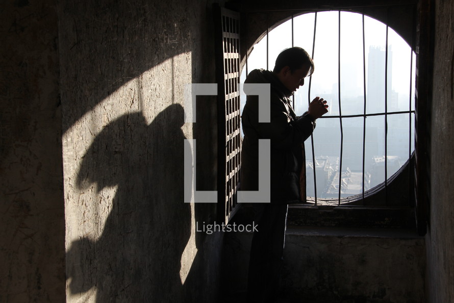 Chinese church leader standing in front of a barred window praying
