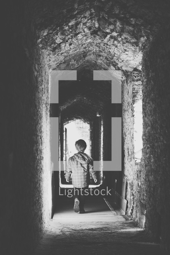 a little boy walking down a stone hallway 