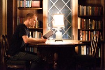 a man reading a book at a table in a library 
