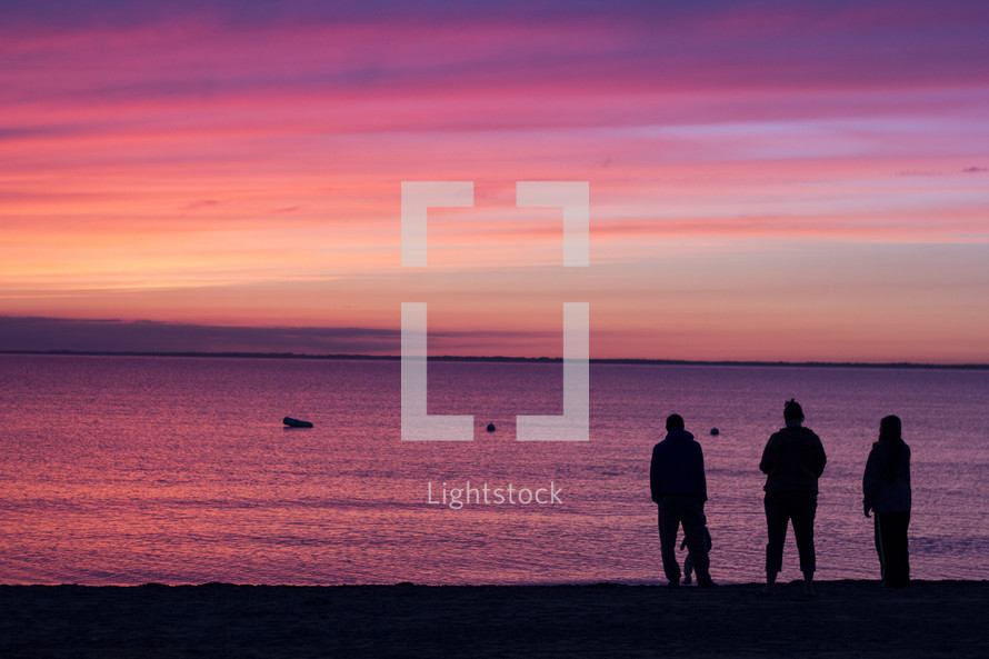 silhouettes of a family standing on a beach at sunset 