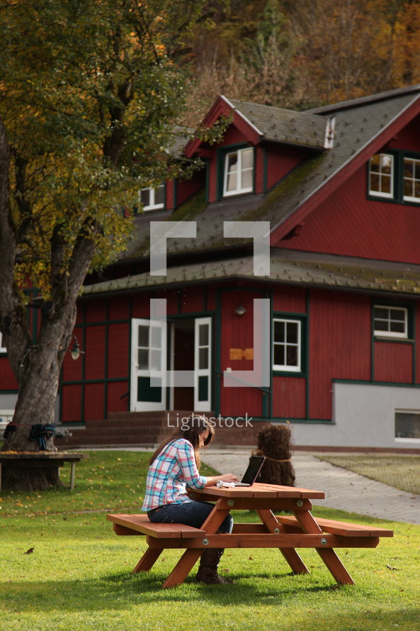 woman studying at a picnic table and a red house