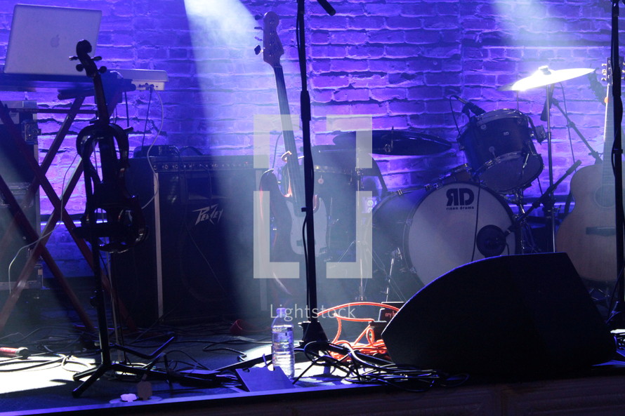drum set, microphones, and guitar on stage under spot lights 