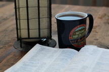 lantern, Bible, and coffee mug on a picnic table at camp 