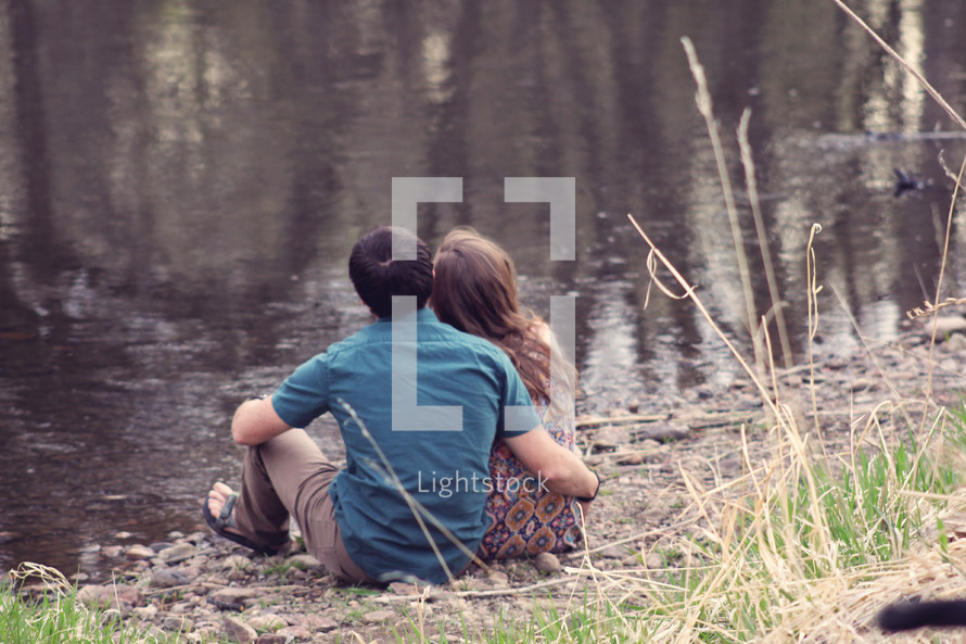 a couple sitting at the edge of a pond 