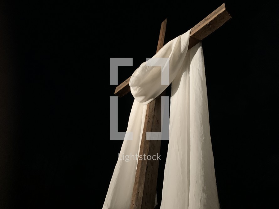 white shroud draped over a cross at night 