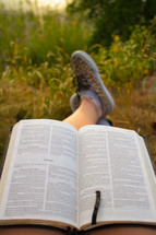 feet of a man reading a Bible outdoors 