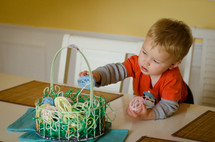 a toddler boy playing with an Easter basket on a table 
