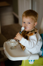 a toddler boy eating yogurt in a highchair 