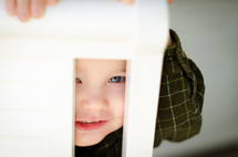 a toddler boy peeking through the slates of a chair 