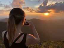 a woman taking a picture of the setting sun 