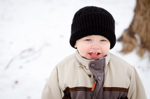a smiling toddler boy in a coat in the snow