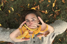 a girl lying in grass playing in fall leaves 
