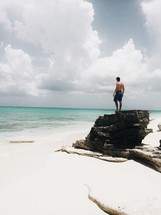 man standing on a rock on a white sand beach 